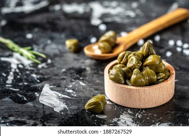 Marinated capers in a woden bowl. Edible flower buds of Capparis spinosa, caper bush or Flinders rose on a dark background.