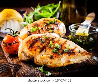 Marinated Grilled Healthy Chicken Breasts Cooked On A Summer BBQ And Served With Fresh Herbs And Lemon Juice On A Wooden Board, Close Up View