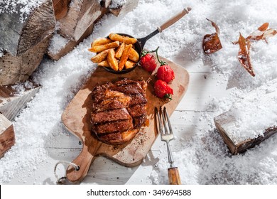 Marinated grilled rib-eye steak and roasted vegetables cooked on a winter barbecue served on a wooden board outdoor in snow, high angle view
