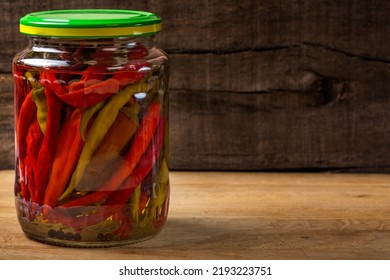 Marinated hot peppers in jar over wooden background