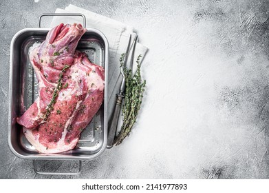 Marinated mutton lamb whole shoulder, raw meat in a steel tray with herbs and spices. White background. Top view. Copy space.