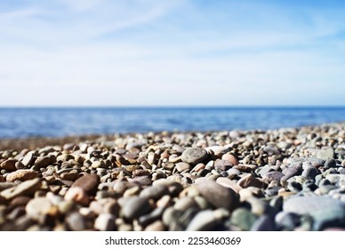 Marine background. Pebble beach on a sunny day. Pebbles close-up, sea and sky in summer without people, soft selective focus - Shutterstock ID 2253460369