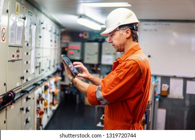 Marine chief engineer watching digital tablet in engine control room. Internet and home connection at sea.