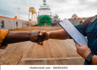 marine contractor businessman handshaking with worker on the ship with contract agreement. Handshake of two boilersuits with different colors wiyh maritime background