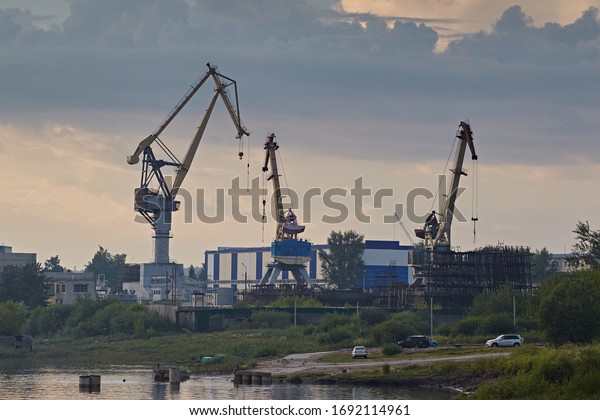 Marine cranes in the port against the sky and the\
shore with cars