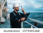 Marine Deck Officer or Chief mate on deck of offshore vessel or ship , wearing PPE personal protective equipment - helmet, coverall. He holds VHF walkie-talkie radio in hands.