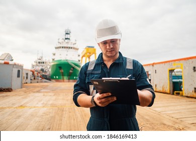 Marine Deck Officer or Chief mate on deck of offshore vessel or ship doing check and filling checklist. Paperwork at sea. Ship is on background