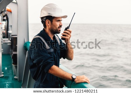 Marine Deck Officer or Chief mate on deck of vessel or ship . He holds VHF walkie-talkie radio in hands. Ship communication
