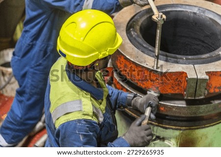 Marine engineer inspecting main engine exhaust valve on board a cargo ship, industrial engine room scene with safety helmet.
