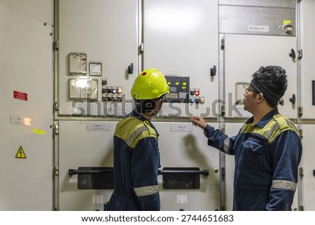 Marine engineers operating the generator control panel inside the engine room, monitoring onboard power production on a commercial vessel.