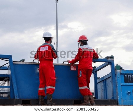 A marine surveyor is looking at the rigger Stevedore who is carrying out a cargo operation with a shore crane to be loaded on the ship