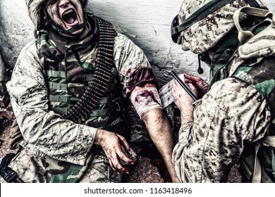 Marine wounded in shoulder, suffering of pain and screaming while receiving medical aid from comrade. Military medic apply pressure bandage to casualty, binding gunshot wound, trying stop bleeding