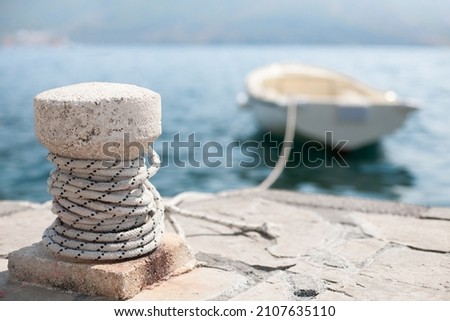 Maritime mooring rope on concrete bollard, close-up. Boat moored at the pier, selective focus.