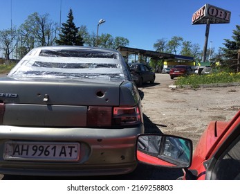 Mariupol, Ukraine, May 20 2022. Partially Broken Car, Pierced By Shell Fragments Stands In Line For Refueling On A Gas Station Near The OBI Banner.