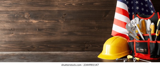 Mark the importance of construction workers on Labor Day. Side view photo of american flag, toolkit, work helmet on wooden background with empty space for promo or message - Shutterstock ID 2344981147