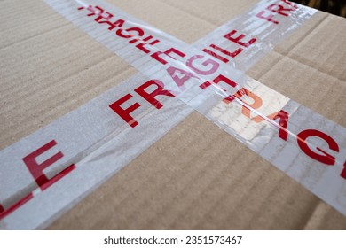 Marked fragile, a cardboard package wrapped in white tape with red writing warning that the package contains something fragile