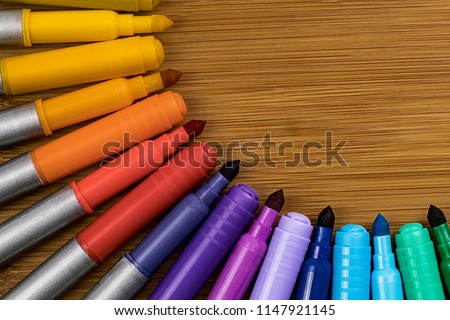 Markers Alternating between Tips and Caps in a quarter circle design on a bamboo table with room on the top right for copy work.  Arranged in the order of the color wheel.