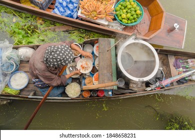Market woman cooking noodle at Damnoen Saduak Floating Market or Amphawa. Local people sell fruits, traditional food on boats in canal, Ratchaburi District, Thailand. Famous Asian tourist attraction.