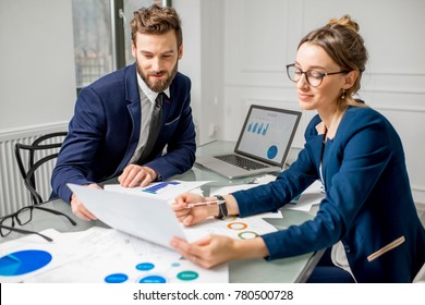 Marketer or analityc manager team dressed in suits working with paper charts and laptops at the white office interior - Powered by Shutterstock