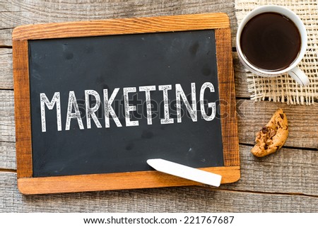Marketing handwritten with white chalk on a blackboard, cup of coffee and biscuit on a wooden background 