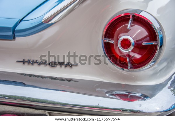 Markham,\
Ontario / Canada – September 9, 2018: A closeup of the shiny chrome\
badge / emblem, rear tail light, and chrome bumper on a vintage\
classic blue and white 1960 Buick\
Invicta.