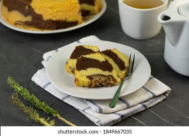 Marmer Cake Or Marbel Cake On White Ceramic On Ceramic White Plate With A Fork, Served With A Cup Of Tea. Black Marble Background. Selective Focus.