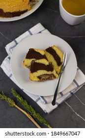 Marmer Cake Or Marbel Cake On White Ceramic Plate, Served With A Cup Of Tea. Black Marble Background. Top View.