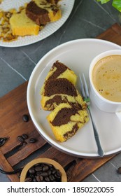 Marmer Cake Or Marbel Cake On White Ceramic On Ceramic White Plate With A Fork, Served With A Cup Of Coffee. Black Marble Background. Selective Focus.