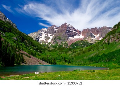 Maroon Bells Mountain Peaks in the summer with Marron Lake in foreground and two hikers on edge of lake - Powered by Shutterstock