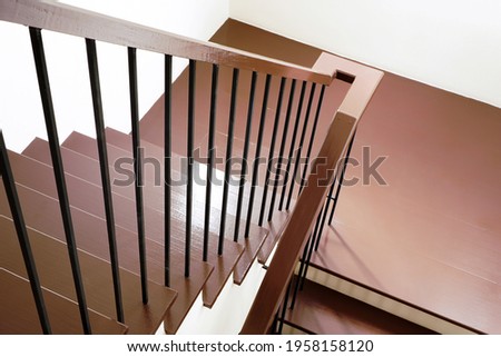Maroon wooden stairs with black steel banister in modern and minimal style with white wall of staircase hall  ,top view from upstairs , selective focus on the steps