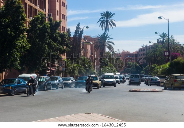 MARRAKESH,\
MOROCCO - APRIL 12 2010: Motorized traffic with emissions inside\
the inner city of Marrakech with cars, mopeds motorcycles and\
pedestrians. Left and right hotels and\
houses