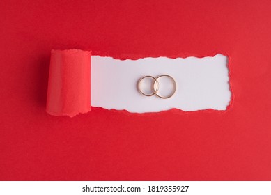 Marriage concept. Top above overhead view photo of two different size rings on torn red paper over white background with copyspace