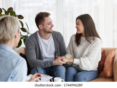 Marriage Reconciliation. Happy Couple Holding Hands Reconciling After Marital Therapy With Female Psychotherapist Sitting On Couch In Office. Selective Focus