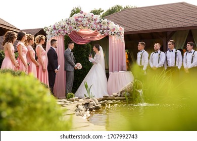 Marriage vow, the bride makes a promise to the groom during the wedding ceremony in the presence of the bridesmaids and groomsmen near beautiful wedding arch