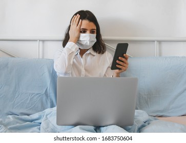 married brunette with a medical mask on her face working or studying from home, sitting in her bedroom in bed with a laptop and smartphone
