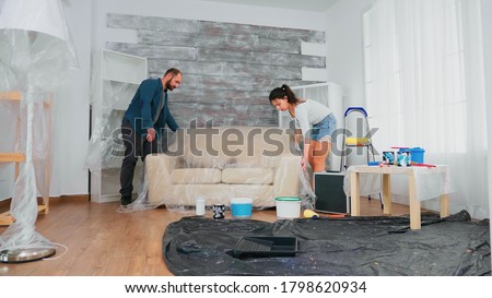 Married couple covering sofa with plastic sheet for home decorating. Apartment redecoration and home construction while renovating and improving. Repair and decorating. Imagine de stoc © 