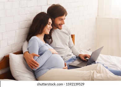 Married couple expecting baby and using laptop at home, watching movie or browsing social media