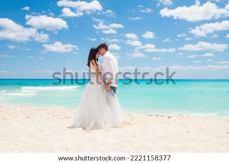 A married couple holding their hands and looking into their eyes. A wedding on the beach-shore. Honey moon on the paradise island. White sand, turquoise sea waters. 