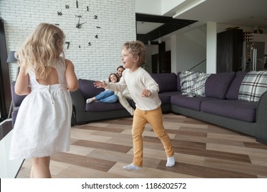 Married Couple With Kids In Living Room At Home. Parents Sitting On Couch And Looking At Playful Joyful Little Preschool Children. Happy Family, Wealthy New House, Buy Real Estate And Mortgage Concept