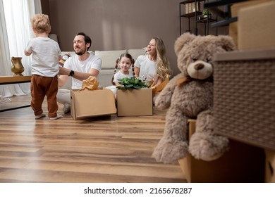 Married couple is in the process of moving, they are sitting in their new apartment, slowly unpacking boxes of belongings with their children talking, laughing, enjoying the change of place - Powered by Shutterstock