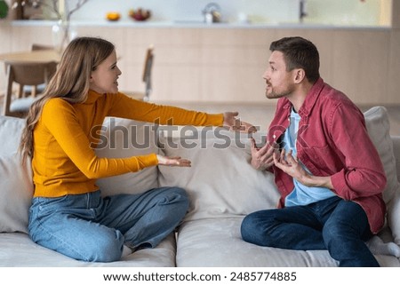Married couple spouses quarrel, squabbling, fighting, vigorously gesticulating while sitting on couch. Aggressive wife blaming husband making excuses. Guy and girl violently discussing acute issue.