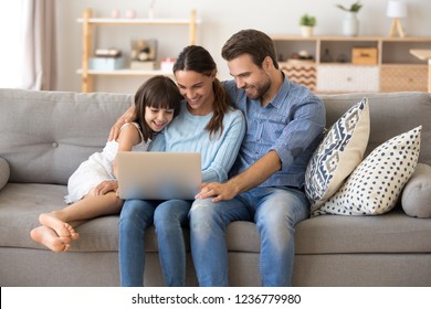 Married Diverse Couple And Little Preschool Daughter Sitting On Couch Using Computer Watching Movie Cartoons Online Surfing Internet Shopping Purchasing Via Internet Spending Weekend Together At Home