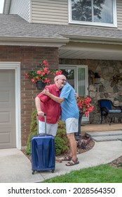 Married Elderly Gay Couple Hug Good-bye Outside Their House As One Of Them Has A Suitcase And Is Getting Ready To Leave.