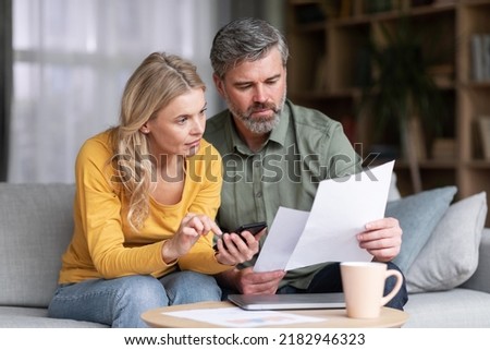 Married Middle Aged Couple Planning Budget Together, Reading Papers And Calculating Spends While Sitting On Couch In Living Room, Husband And Wife Checking Documents And Accounting Taxes, Closeup Foto stock © 