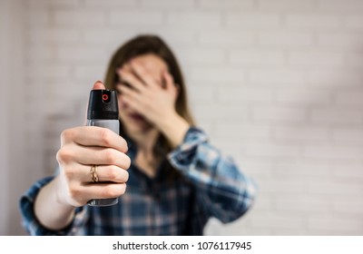 Married woman is holding pepper spray canister for personal protection. Girl covers her face with hands. White background behind. Self-defense photo. Copy space place.