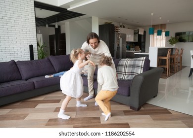 Married Young Couple With Little Children Spend Free Time In Living Room At Wealthy New Home. Mother Sits On Sofa Smiling Father Playing With Preschool Son And Daughter. Happy Family Together Concept