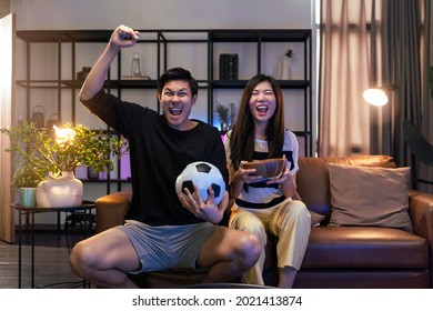 marry adult asian watching TV at home ,asian couple cheering sport games competition together with laugh smile victory on sofa couch at living room home isolation activity