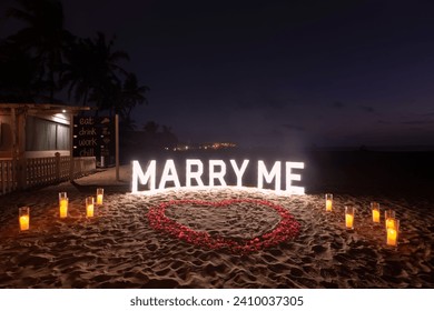 Marry me proposal decoration lights with heart shaped flower petals on sand