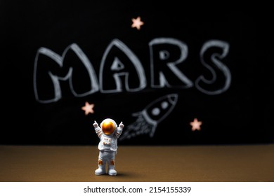 Mars colonization. Figure of astronaut with victoriously raised hands. In the background, a chalky black board with the inscription MARS.