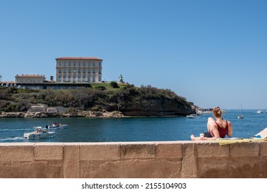 Marseille, France  -16 April 202: .A young woman is seen on back, sunbathing on the wall of the Fort Saint Jean in Marseille, facing the Palais du Pharo